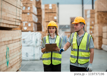 Team engineer carpenter wearing safety uniform and hard hat working holding clipboard checking quality of wooden products at workshop manufacturing. man and woman worker wood warehouse industry. 119737196