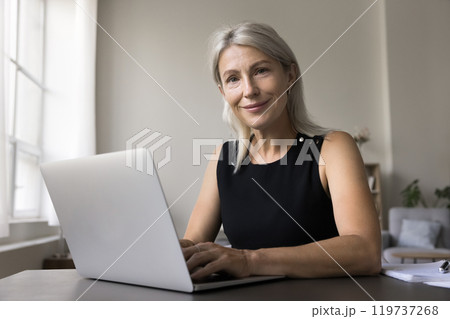 Portrait smiling confident old lady sit at desk by laptop Portrait smiling confident old lady sit at desk by laptop 119737268