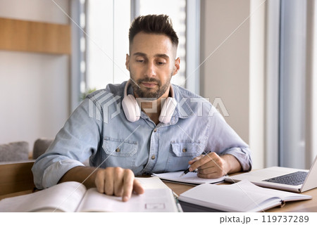 Focused adult Latin student man reading learning textbook at home 119737289