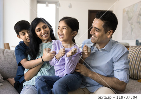 Happy loving Indian parents and brother tickling little girl 119737304