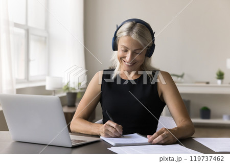 Diligent mature female in earphones engaged in e-learning on laptop 119737462