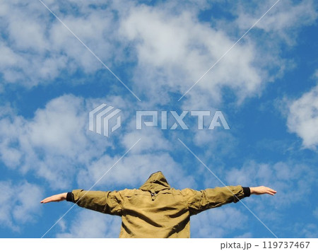 person in green hoodie from the back with head down and arms outstretched in pose of flying in blue sky with clouds, human emotions of different spectrum with image of flight 119737467