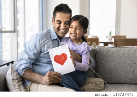 Happy Indian dad holding greeting card and daughter in arms Happy Indian dad holding greeting card and daughter in arms 119737473