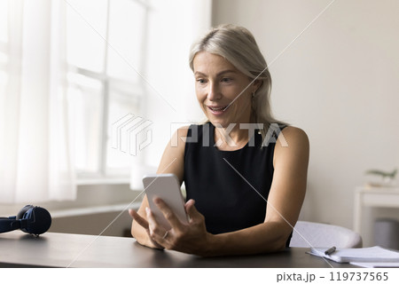 Amazed older woman sit at desk look on phone screen Amazed older woman sit at desk look on phone screen 119737565