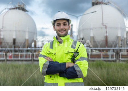 Portrait success man professional engineer technician smiling wear safety uniform and white hard hat arms crossed looking at camera stand area near tank refining oil petrochemical industry factory. Portrait success man professional engineer technician smiling wear safety uniform and white hard hat arms crossed looking at camera stand area near tank refining oil petrochemical industry factory. 119738143
