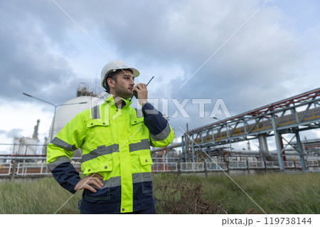 Man professional engineer technician wear safety uniform and white hard hat working area near tank refining oil petrochemical industry factory. Industrial factory site energy power station. Man professional engineer technician wear safety uniform and white hard hat working area near tank refining oil petrochemical industry factory. Industrial factory site energy power station. 119738144