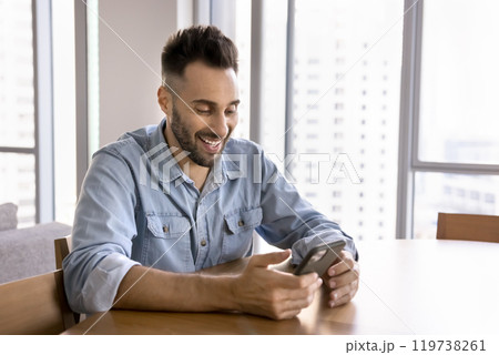 Cheerful handsome Hispanic man playing online game on smartphone 119738261