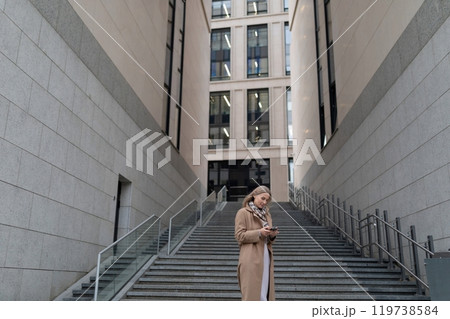 A businesswoman stands on the steps near a business center, checking her phone A businesswoman stands on the steps near a business center, checking her phone 119738584