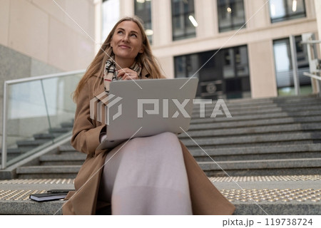 Business woman working on a laptop outside a modern business center during the daytime while sitting 119738724