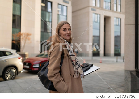 Business woman in a stylish coat walking near a modern business center on a sunny afternoon Business woman in a stylish coat walking near a modern business center on a sunny afternoon 119738756