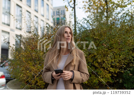 A businesswoman looks away from her phone and towards a business center, thinking about her next 119739352