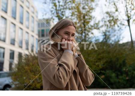 A businesswoman stands outside a business center, adjusting her coat in the cool fall weather 119739426