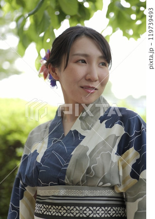 緑の木の葉に立つ若い浴衣の女性 119739493