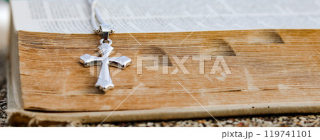 Shiny metal cross leaning against an old open book symbolizing the spread of Jesus Christs love among Christians reflecting faith devotion and the importance of Christian teachings. Shiny metal cross leaning against an old open book symbolizing the spread of Jesus Christs love among Christians reflecting faith devotion and the importance of Christian teachings. 119741101