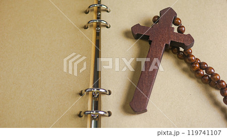 Dark red wooden cross leaning against an old open book symbolizing the spread of Jesus Christs love among Christians reflecting faith devotion and the importance of Christian teachings. Dark red wooden cross leaning against an old open book symbolizing the spread of Jesus Christs love among Christians reflecting faith devotion and the importance of Christian teachings. 119741107