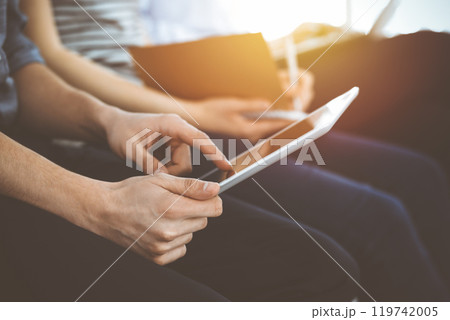 Group of casual dressed business people working at meeting or conference in sunny office, close-up of hands. Businessman using tablet computer Group of casual dressed business people working at meeting or conference in sunny office, close-up of hands. Businessman using tablet computer 119742005