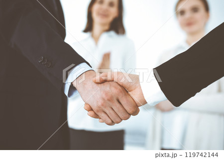 Businessman and woman shaking hands with colleagues at the background. Handshake at meeting in office. Concept of success in business 119742144