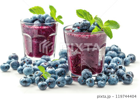 Two glasses of vibrant blueberry smoothies adorned with fresh mint leaves and surrounded by scattered berries 119744404