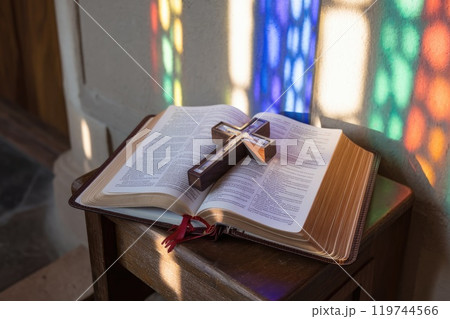 Wooden cross resting on open bible in church with stained glass window light Wooden cross resting on open bible in church with stained glass window light 119744566