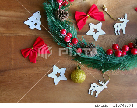 Wooden ornaments, a wreath from a Christmas tree, berries and bows lie on the wooden surface. New Year and Christmas decor. Preparing for the holiday. Woody background 119745371