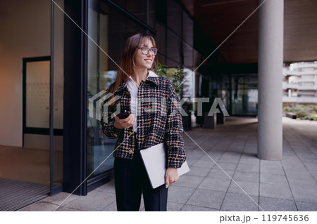 A Professional Woman in a Modern Office Environment Holding a Cup of Coffee and a Laptop 119745636