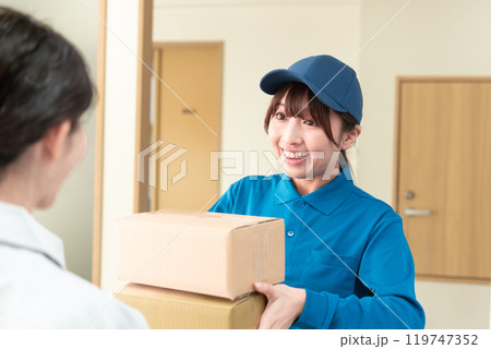 宅配便の荷物を受け取る作業着姿の若い女性と宅配業者の女性 宅配便の荷物を受け取る作業着姿の若い女性と宅配業者の女性 119747352