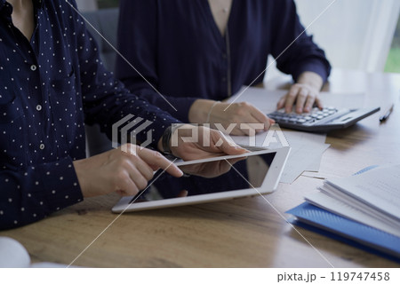 Accountants or auditors reviewing financial documents while sitting at the wooden desk in office. Professionals are analyzing paper reports using tablet computer, close up. Audit and taxes 119747458