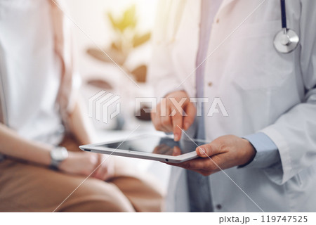 Doctor and patient in clinic. Friendly physician using tablet computer near a young woman. Medicine concept Doctor and patient in clinic. Friendly physician using tablet computer near a young woman. Medicine concept 119747525
