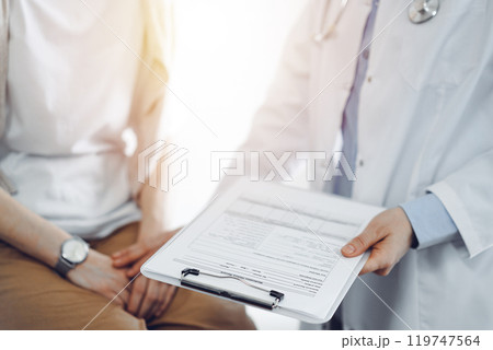 Doctor and patient in clinic. Friendly physician examining a young woman with a one hand while keeping a clipboard with medical records in another. Medicine concept 119747564