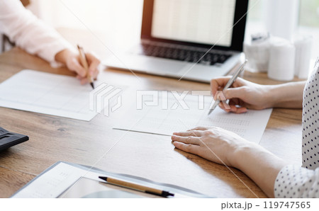 Two accountants using a laptop computer and calculator while counting taxes at wooden desk in office. Teamwork in business audit and finance 119747565