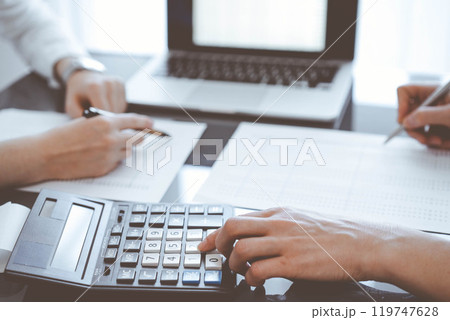 Two accountants use a calculator and laptop computer for counting taxes or revenue balance. Business, audit, and taxes concepts Two accountants use a calculator and laptop computer for counting taxes or revenue balance. Business, audit, and taxes concepts 119747628
