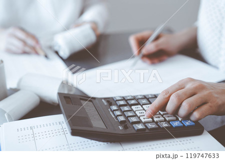Two accountants use a calculator and laptop computer for counting taxes or revenue balance. Business, audit, and taxes concepts 119747633