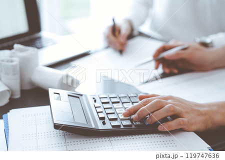 Two accountants use a calculator and laptop computer for counting taxes or revenue balance. Business, audit, and taxes concepts Two accountants use a calculator and laptop computer for counting taxes or revenue balance. Business, audit, and taxes concepts 119747636