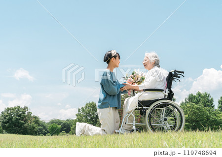 車椅子に乗るおばあちゃんに花束をプレゼントする笑顔の孫娘 119748694