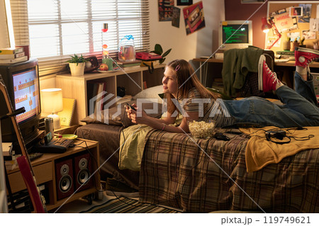 Young Woman Relaxing in Cozy Bedroom Playing Video Game 119749621