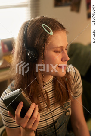Smiling Woman Holding Device While Listening to Music 119749647