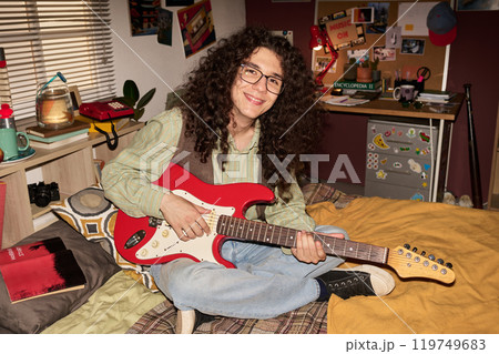 Smiling Youth Holding Electric Guitar in Cozy Bedroom 119749683