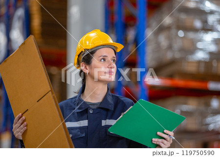 Female warehouse worker holding paper product and clipboard checking inspecting quality cardboard corrugated carton in storage. Large industry in paper product line manufacturing. Female warehouse worker holding paper product and clipboard checking inspecting quality cardboard corrugated carton in storage. Large industry in paper product line manufacturing. 119750590
