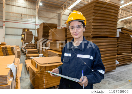 portrait of woman paper warehouse worker holding clipboard looking at camera. Employees warehouse checking quality cardboard in storage. Large industry in paper product line manufacturing. portrait of woman paper warehouse worker holding clipboard looking at camera. Employees warehouse checking quality cardboard in storage. Large industry in paper product line manufacturing. 119750903