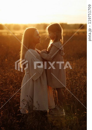 Woman and child standing in a field at sunset Woman and child standing in a field at sunset 119751709
