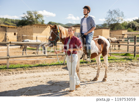 Young woman leading horse with man riding Young woman leading horse with man riding 119753059