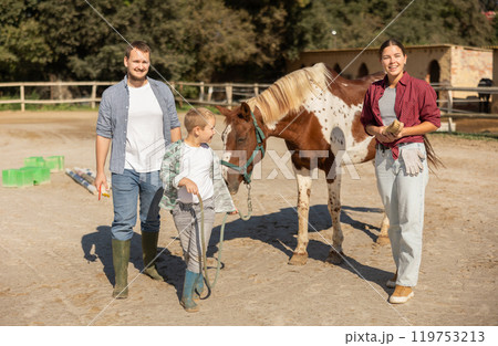 Boy leads horse by leash in paddock Boy leads horse by leash in paddock 119753213