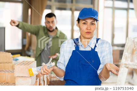 Confused female builder in building under construction with angry customer Confused female builder in building under construction with angry customer 119753340