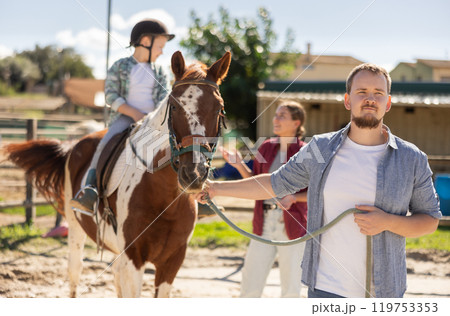 Young man leading horse with boy on horseback 119753353