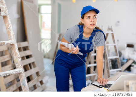 Woman worker checking documents and using laptop in construction site Woman worker checking documents and using laptop in construction site 119753488