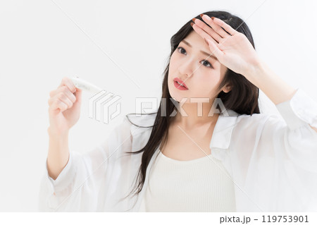 体温計を見ながら額に手を当てている若い女性 119753901