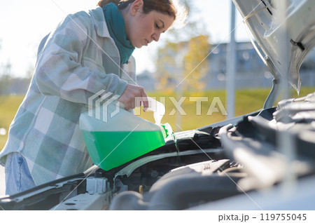 Caucasian woman filling car reservoir with windshield washer fluid from bottle.  119755045