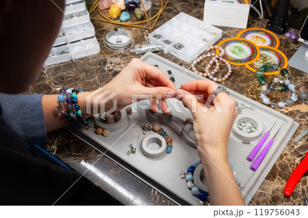 Caucasian woman assembles handmade jewelry bracelets made of stones and metal in her workshop with dark lighting and mysterious atmosphere 119756043