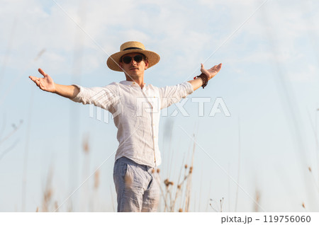 Side view of a young Jewish man in a straw hat and white shirt, proudly looking out over a field, arms outstretched, feeling free Side view of a young Jewish man in a straw hat and white shirt, proudly looking out over a field, arms outstretched, feeling free 119756060