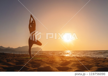 Vrikshasana tree pose from yoga, female silhouette at sunset or sunrise. Back view of a girl practicing morning workout on the seashore Vrikshasana tree pose from yoga, female silhouette at sunset or sunrise. Back view of a girl practicing morning workout on the seashore 119756090